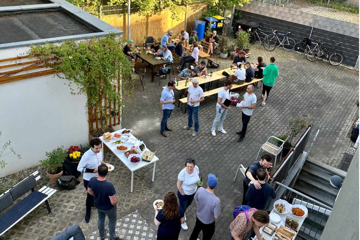 Fröhliche Teamfeier im Freien auf dem Hof des Studio Delta Coworking. Das Team genießt gemeinsames Essen, Getränke und Gespräche in ungezwungener Atmosphäre.